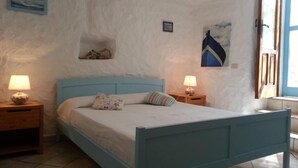 A bedroom with a blue bed frame, two bedside tables with lamps, a small shelf with a decorative item, and a window with a view of the sea. - The house by the sea one step away from the beach (ponza)