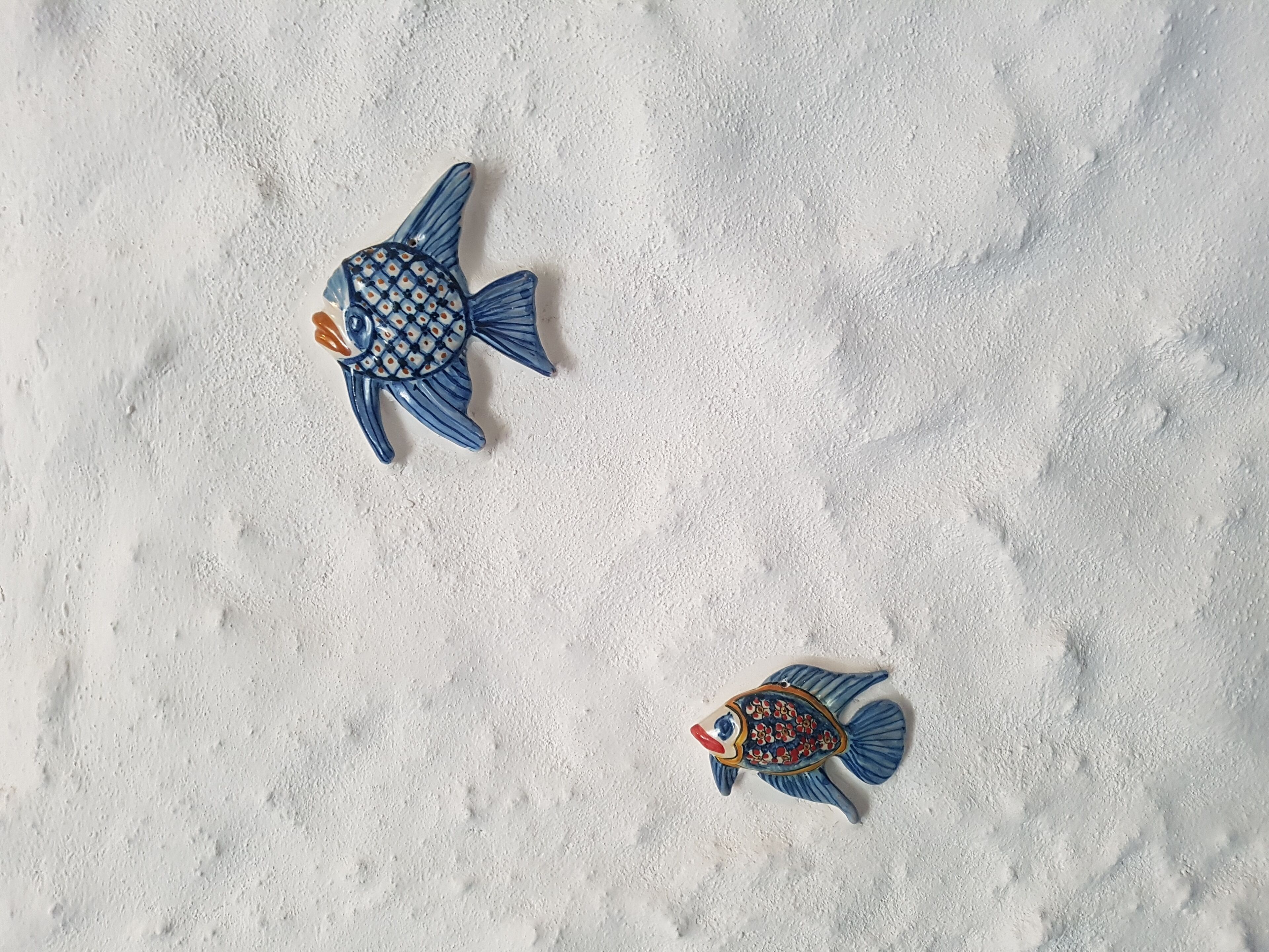 Two ceramic fish on a textured white surface.