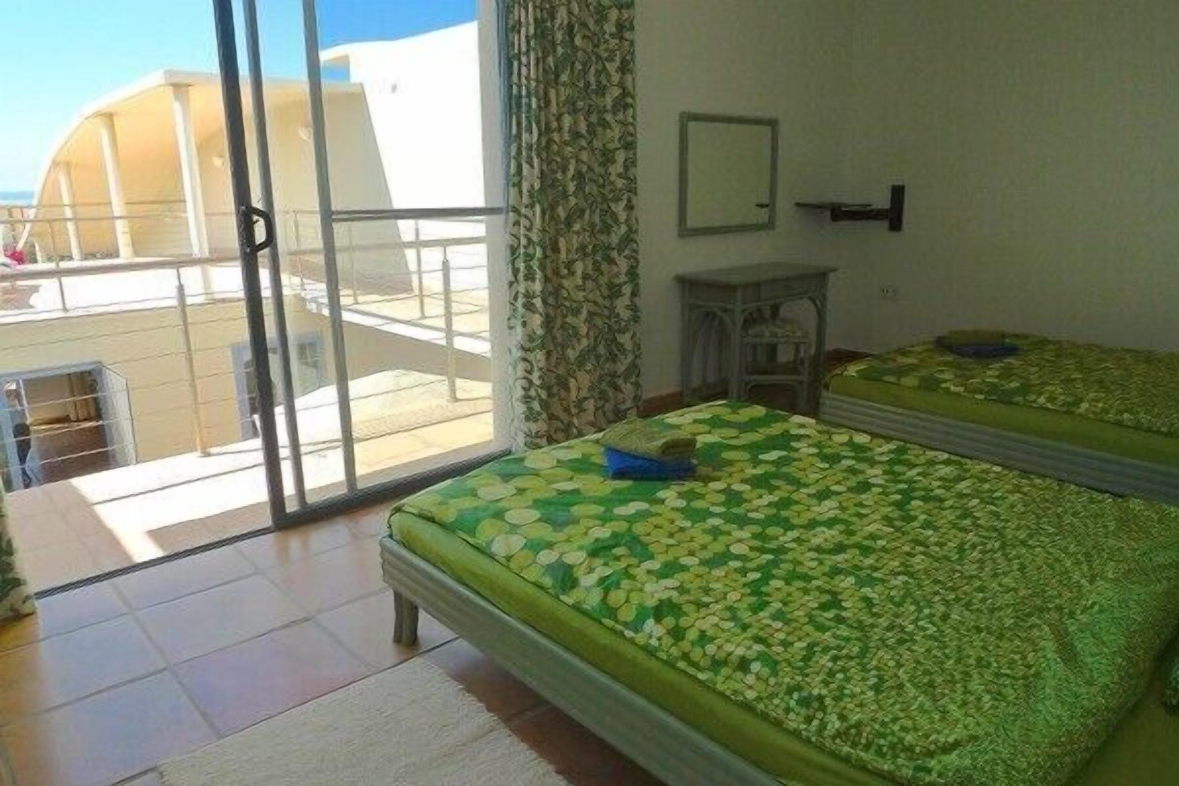A hotel room with two beds, a balcony, a small table, and a mirror.