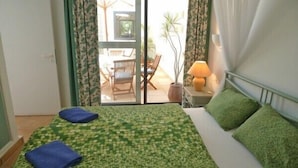 A hotel room with a bed, a nightstand, a lamp, and a view of an outdoor seating area.