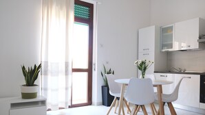 A modern kitchen with white cabinets, a dining area with a white table and chairs, and a potted plant on a white console table. - 100 meter from the sea, nice apartment in centre of Alghero with terrace  (Alghero)