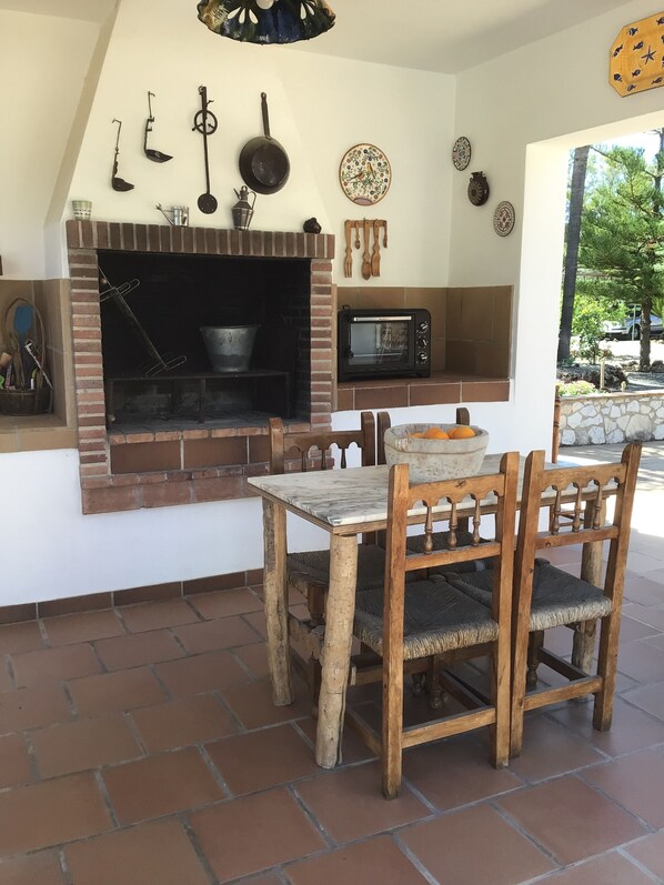 A brick fireplace with a microwave above it, wooden chairs, and a table with a bowl of oranges.