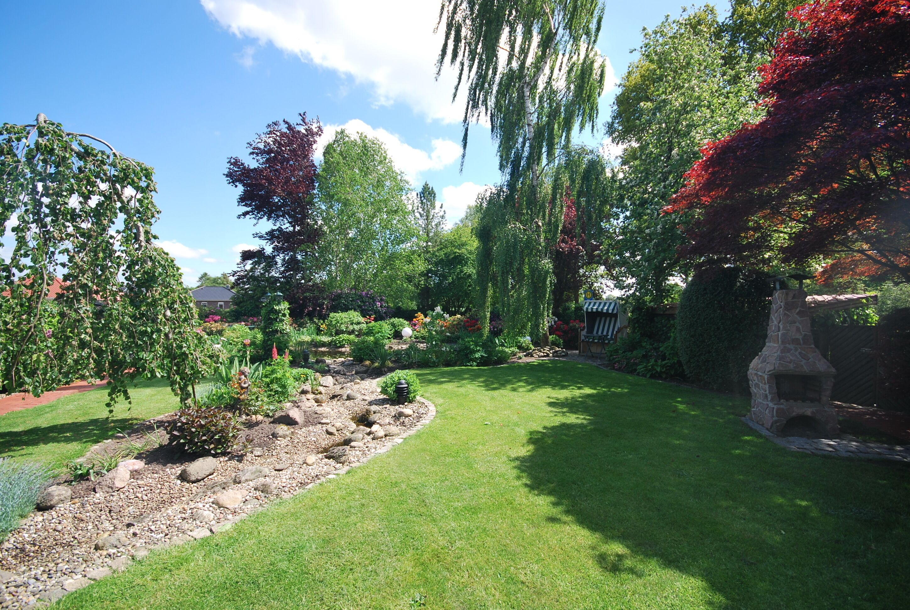 A well-maintained garden with a variety of trees, a stone fireplace, and a clear sky.