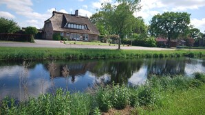 A traditional house with a thatched roof, a pond in the foreground, and a well-maintained garden. - 4 * holiday on the canal in Nordgeorgsfehn (East Frisia) (Uplengen)