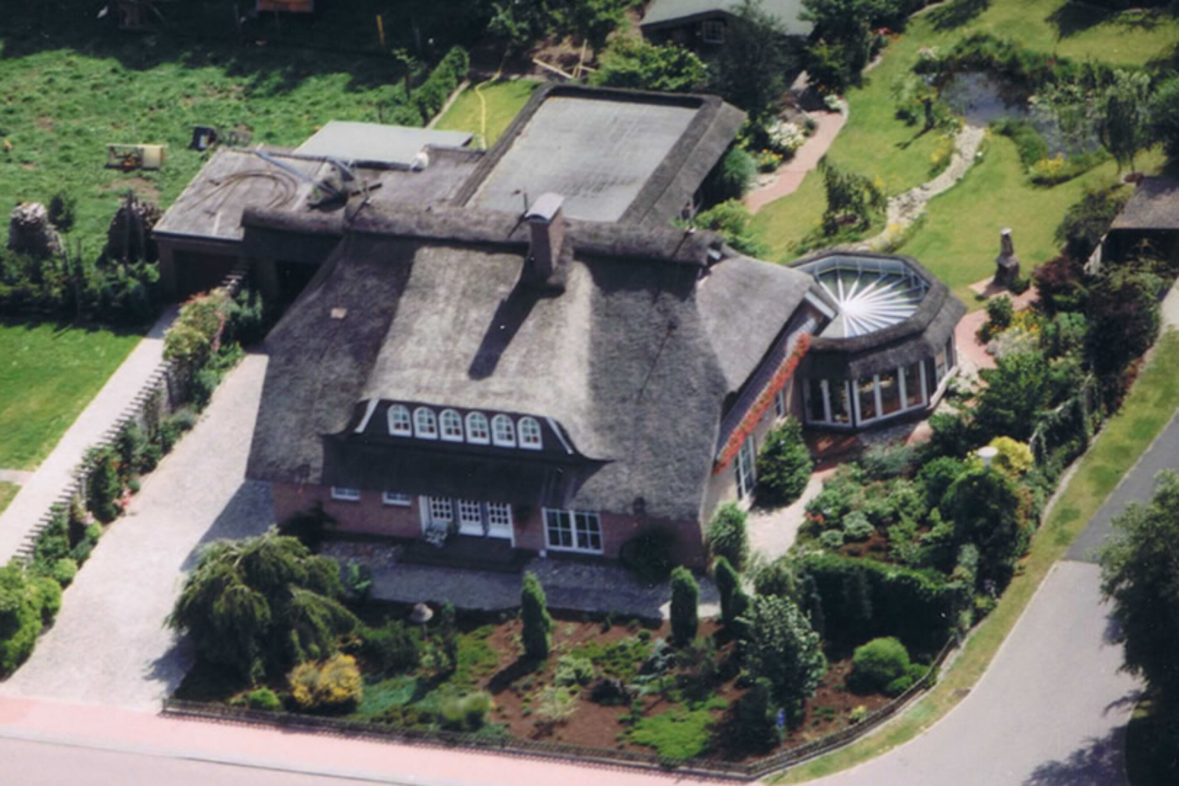 Una vista aerea di una grande casa storica con una torre circolare imponente, circondata da giardini curati e un vialetto lastricato.