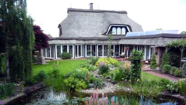 A large house with a thatched roof, surrounded by a well-maintained garden with a pond and various plants. - 4 * holiday on the canal in Nordgeorgsfehn (East Frisia) (Uplengen)