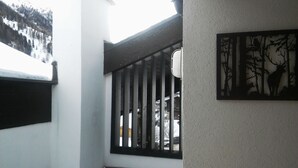 A view of a building's exterior with a metal gate, a wall-mounted picture of a forest scene, and a snowy mountain in the background. - Luxurious and large apartment (103 m²) at 1,735 m with underground parkin (Haute Nendaz / Siviez)