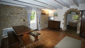 Una habitación rústica con pared de piedra, una mesa de madera con bancos, un televisor y un arco de piedra.