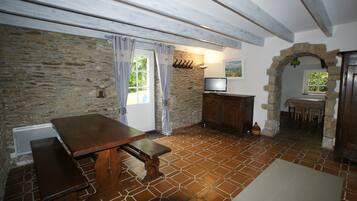 Une pièce rustique avec un mur en pierre, une table en bois avec des bancs, un téléviseur et une arche en pierre.