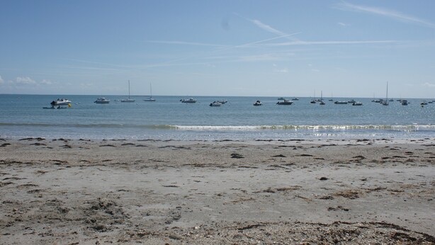 Una playa con barcos anclados en el agua y una orilla arenosa.