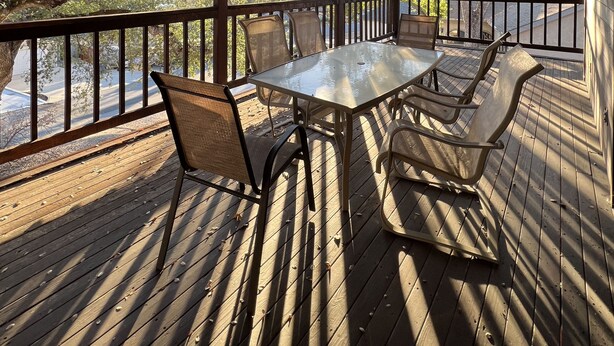 A covered outdoor seating area with a table and chairs, wooden deck, and a view of trees and a road. - What a Great Escape for Families  and Friends!   Private Slip! (Lake Nacimiento)