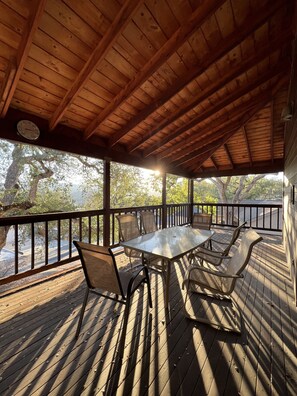 Un espace extérieur aménagé, abrité et doté de tables et de chaises, d’une terrasse en bois et d’une vue sur les arbres et une route.