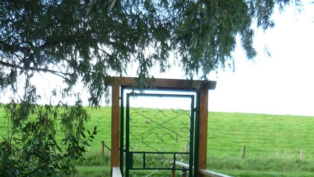 A wooden wooden bridge leading to a metal gate in a grassy field.