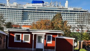 A red building with a white door and windows, in front of a large cruise ship labeled "P&O Cruises."