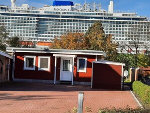 Um edifício vermelho com porta e janelas brancas, em frente a um grande navio de cruzeiro com a inscrição "P&O Cruises".