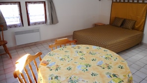Une chambre à coucher avec un lit, une table et des chaises, une fenêtre avec des rideaux et un radiateur.