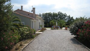 A residential property with a gravel driveway leading to a house with a tiled roof and a chimney. There is a garden with various plants and flowers on the left side. - Holiday home with private pool at the foot of the Pyrenees and near the beach (Laroque-Des-Albères)