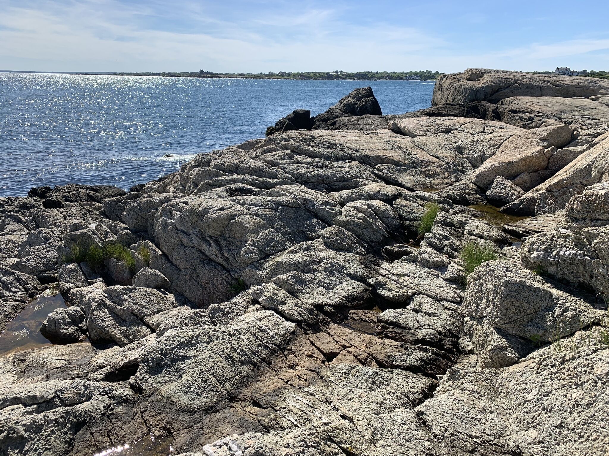 A rocky shoreline with a clear view of the sea and distant buildings.