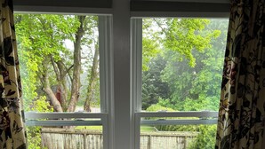 A white sofa with a single white pillow in front of a window with floral curtains.