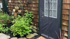 A wooden house with a green door, a small garden with various plants, and a decorative bird sculpture.