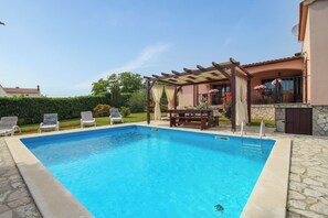 Una piscina rectangular con una pérgola y sillas de descanso en un patio trasero.