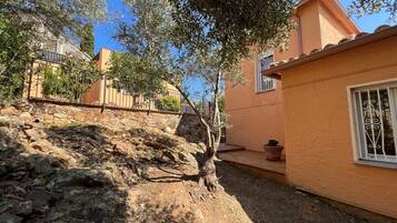 Un patio con muro de piedra, un árbol y un edificio con tejado de tejas.