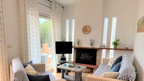 Un salon chaleureux avec des meubles en osier, un téléviseur à écran plat, une cheminée et une vue sur le balcon.