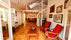 A spacious living area with a wooden floor, a central table, and two red cushioned chairs. A white staircase leads to an upper level. - Villa Emeraude - Superb Creole villa with amazing Pool & direct access to beach (Diamant)
