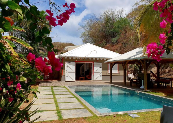 A pool area with a covered seating area and a building with open doors.