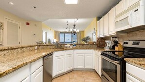 A kitchen with white cabinets, granite countertops, a black stove, and a microwave.