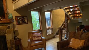 A cozy living room with a stone fireplace, leather armchairs, a wooden floor, and a staircase leading to an upper level.