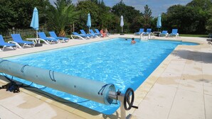 A swimming pool with blue lounge chairs and umbrellas, surrounded by trees.