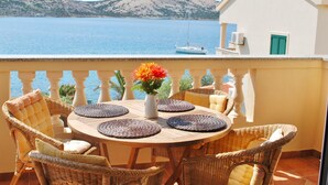 A balcony with wicker chairs, a round table with placemats, and a vase with flowers.