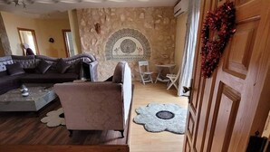 A living room with a stone wall, a fireplace, a sofa, a coffee table, and a wooden door with a wreath. - Vacation apartment in Tunisia (quiet location) (CHATT MERIAM)
