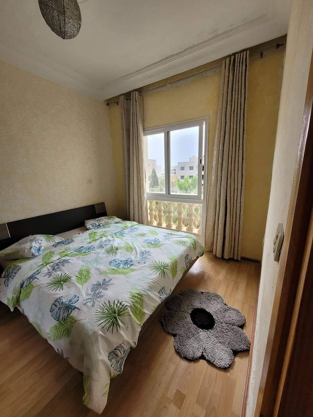 Un dormitorio con cama, ventana con cortinas, suelo de madera y una puerta.