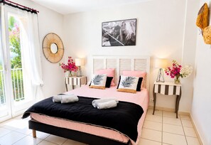 A bedroom with a bed, bedside tables, a wall-mounted fan, a picture, and a window with curtains.