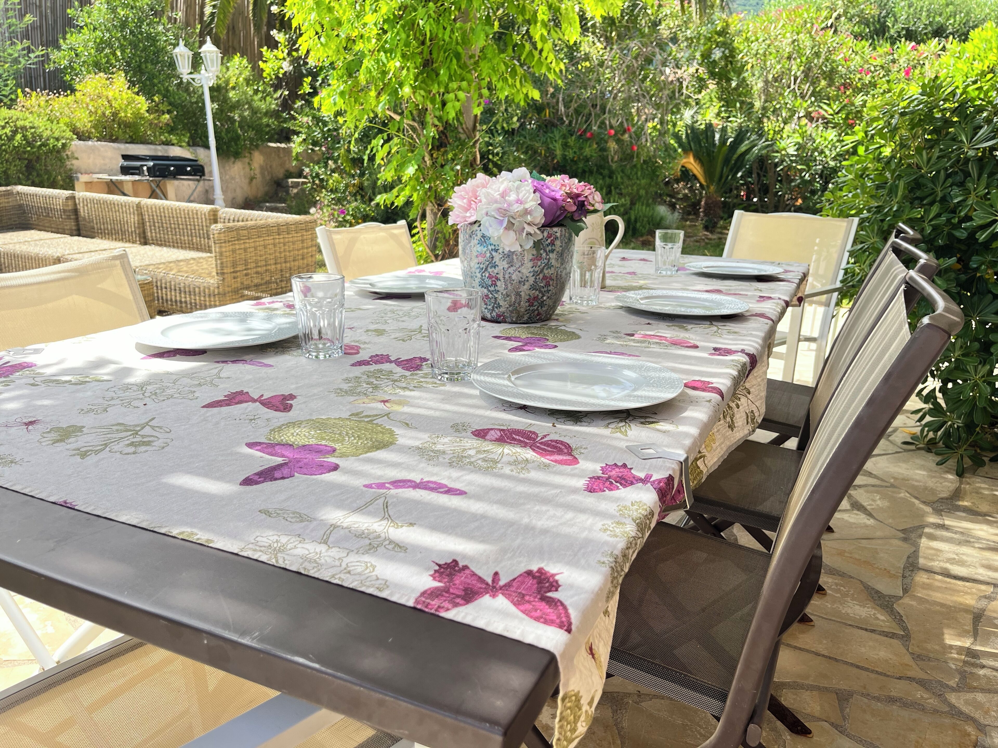 A table set outdoors with a floral tablecloth, surrounded by chairs and a wicker sofa.