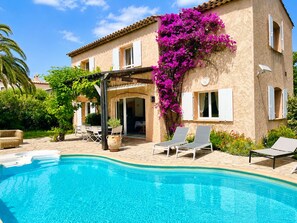 Ein Poolbereich mit Liegestühlen, einer Pergola und einem Gebäude mit einem Ziegeldach und Fensterläden.