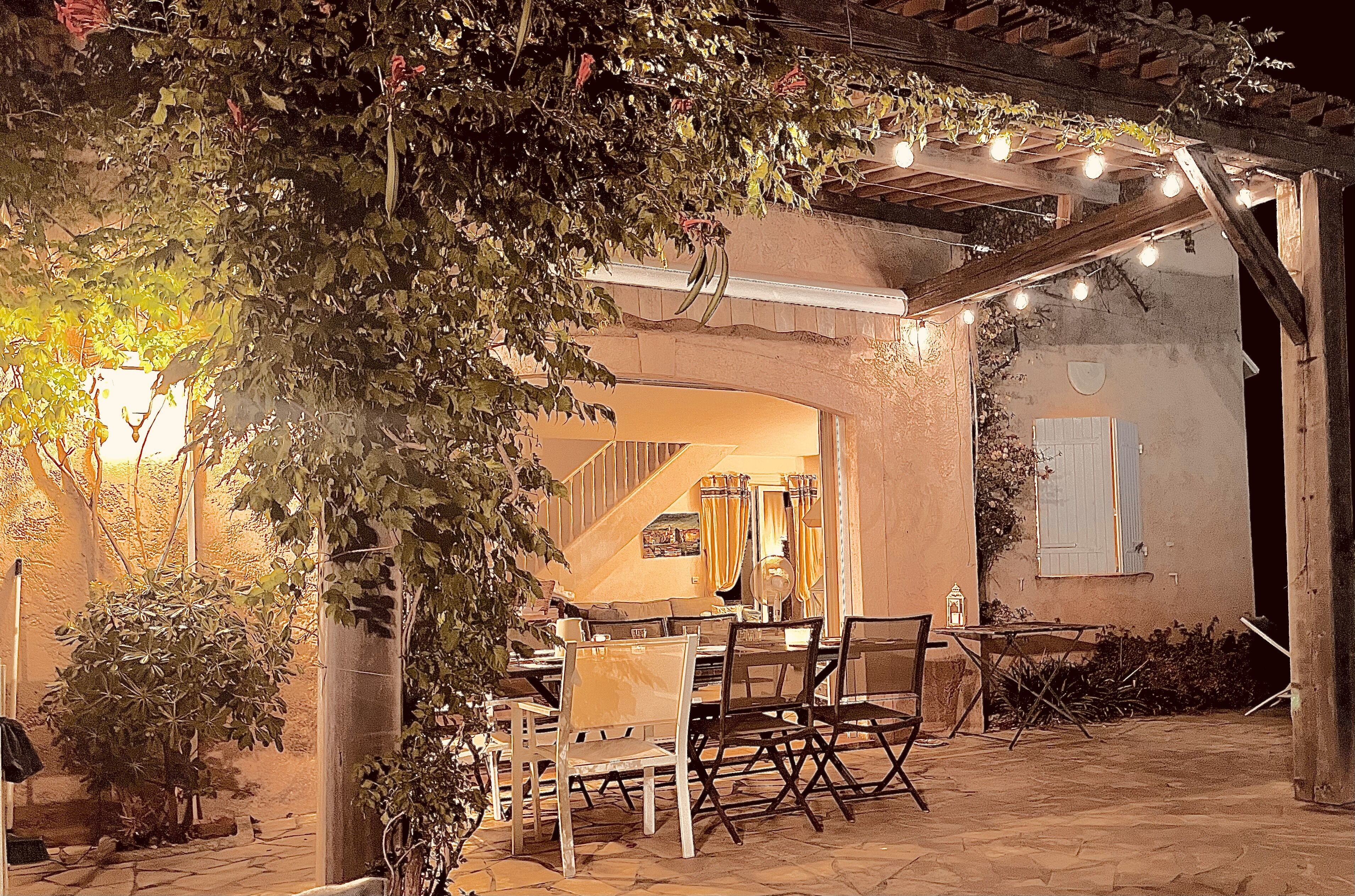 An outdoor patio area with a pergola, string lights, and a dining table with chairs.