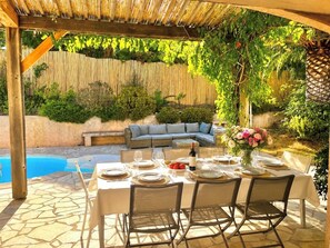 Eine Terrasse im Freien mit Pool, einem Esstisch für vier Personen und einer Couch.