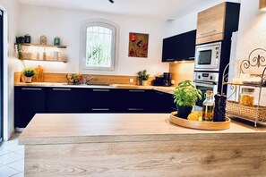 A modern kitchen with black cabinets, a wooden countertop, a large window, and a decorative plant centerpiece.