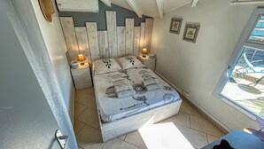 Un dormitorio con una cama, dos mesitas de noche, un ventanal y una puerta.