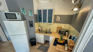 Una cocina compacta con un refrigerador Bosch, microondas, tostadora y pileta. Hay cuadros enmarcados en la pared y un pequeño bote de basura.
