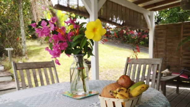 Una mesa con mantel estampado, un florero con flores y una cesta de frutas y pan.