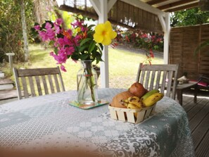 Une table recouverte d’une nappe à motifs, un vase rempli de fleurs et un panier contenant des fruits et du pain.