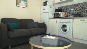 Un espacio habitable compacto con sofá, lavadora, microondas y una pequeña mesa con una caja de pañuelos.
