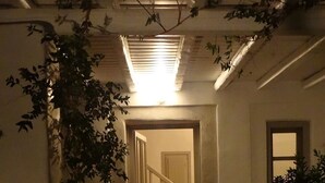 Een gang met een trap die naar een kamer leidt, omgeven door muren en een plafond met blootliggende leidingen.