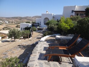 A stone pathway leading to a white building with a view of the countryside. There are lounge chairs and a small tree in the foreground.