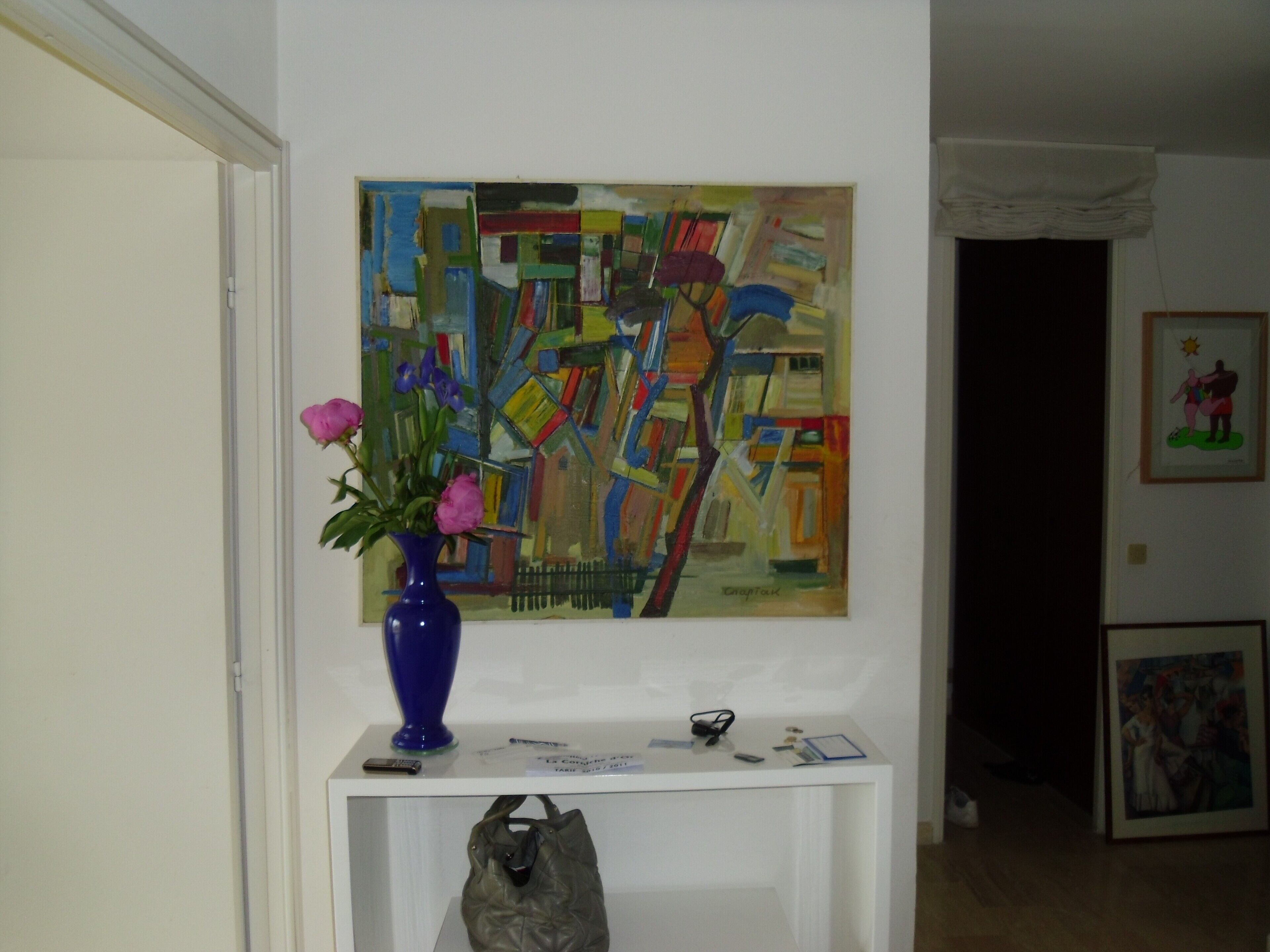 Une pièce comprenant une console blanche sur laquelle sont disposés un vase de fleurs, un tableau et quelques objets personnels.
