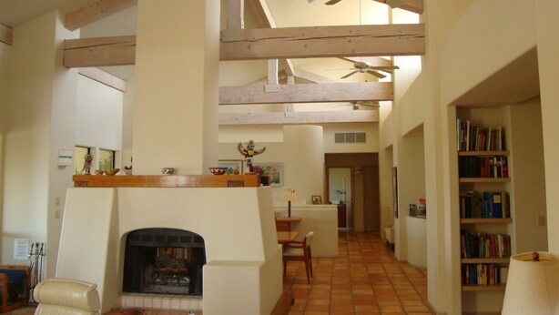 Un salón espacioso con chimenea, techos altos, vigas de madera a la vista y un ventilador de techo.